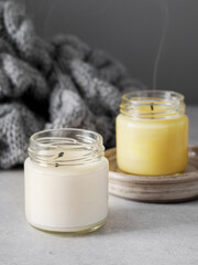Burning candles on grey table, space for text. Grey knitted scarf and scented candles. Cozy winter atmosphere. 2021. Сolors of the year. burning candles on a gray background. New Year. Romantic.