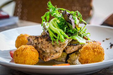 a plate of roast chicken with croquettes, salad and baby tomatoe