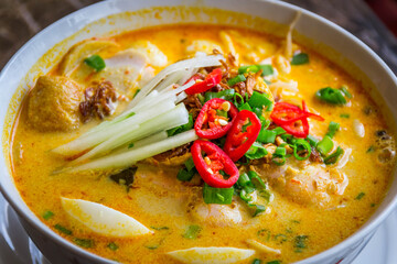 a bowl of laksa rice noodles in mild curry gravy with hard boiled egg bean sprouts, scallions, tofu puffs and fish cake