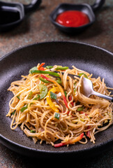 stir fried vegetarian noodles with sauce served in a black plate with fork
