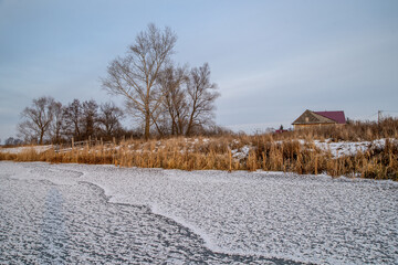 Transparent ice on the lake with snowflakes in the form of stars. Yellow frozen grass. On the shore of the house.