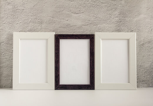 Three empty photo frames in a dark and light frame on a table or shelf with a copy of the place.