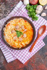 Vertical view of delicious chicken soup with noodles greens and spoon on pink stripped towel oil bottle garlic lemon on dark background stock image