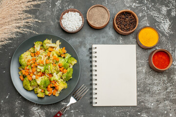 Set of different spices in brown bowls and vegetable salad with fresh broccoli and notebook