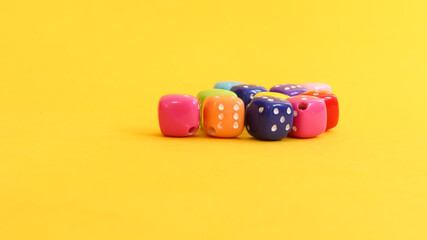 Small dice of various colors on yellow background.