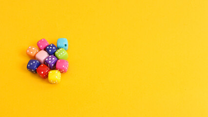 Small dice of various colors on yellow background.