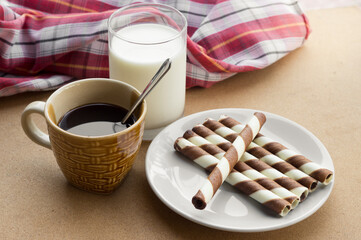 Chocolate wafer rolls with coffee and milk on table.