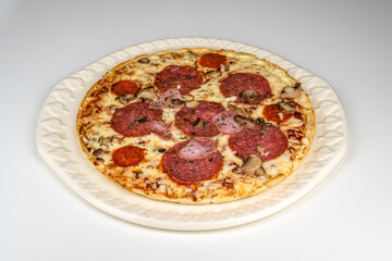 Eine fertig gebackene Pizza mit Salami, Schinken und Käse belegt liegt auf einem runden Teller.