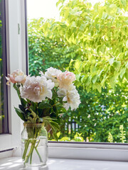 Bouquet of peonies in a vase on a windowsill.