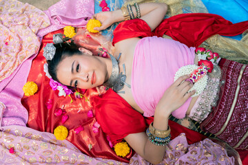 Beautiful Thai woman wearing thai traditional clothing lie down on silk of various colors.