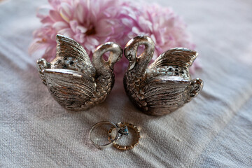 two silver swans, two wedding rings and flowers on a linen napkin on the table