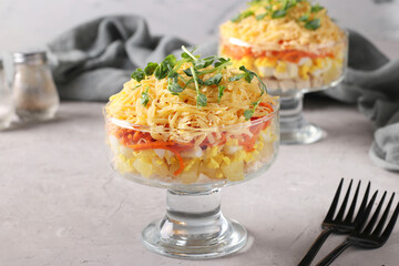 Two servings of puff salad with chicken, cheese, pineapple, egg and carrot on a light gray background. Closeup