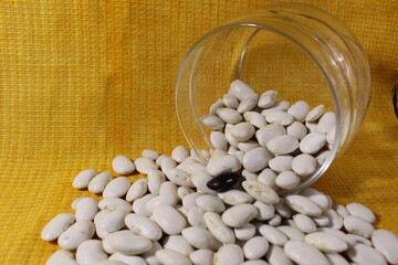 White dry beans in a jar lies spilled out on a yellow lemon background with a copy of the space