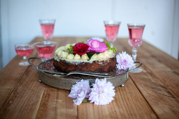 festive cake and rose wine in glasses, flowers on wooden table for birthday