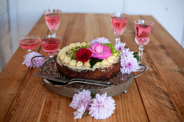 festive cake and rose wine in glasses, flowers on wooden table for birthday