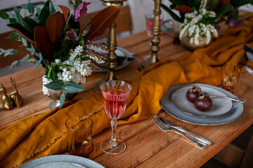 long wooden party table with stylish decoration, with candlesticks, vases of flowers, glasses with wine, plates and food in a room with a white brick wall