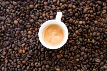 Flat lay with copy space, (selective focus) A white espresso cup with some creamy coffee is placed on some blurred roasted coffee beans.