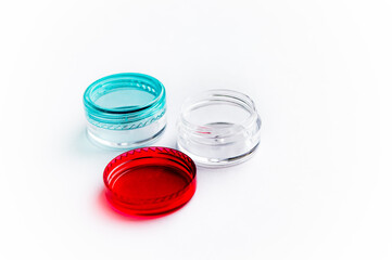 Empty small plastic or glass jars for beauty cream on white background. Transparent containers with a blue and red lids. Acrylic containers for skin care cosmetics.