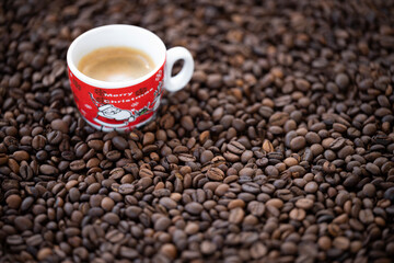 Flat lay with copy space, (selective focus) A Christmas cup with some creamy coffee is placed on some roasted coffee beans.
