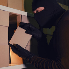 A thief in a black hood steals a parcel in a warehouse in the dark. Concept of problems with theft...