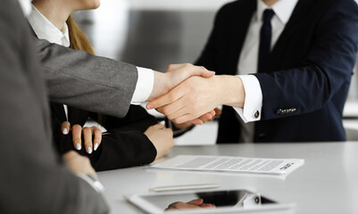 Unknown businessman shaking hands with his colleague or partner above the glass desk in modern office, close-up. Business people group at meeting