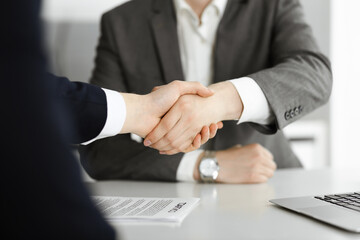 Unknown businessman shaking hands with his colleague or partner above the glass desk in modern office, close-up. Business people group at meeting