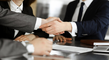 Unknown businessman shaking hands with his colleague or partner above the glass desk in modern office, close-up. Business people group at meeting