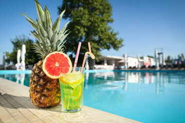 Tasty refreshing cocktail and pineapple on edge of swimming pool. Party items