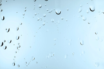 Glass with water drops on light blue background, closeup