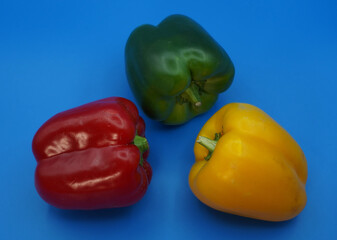 Three paprika peppers: yellow, red and green against a blue background close-up.