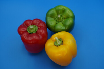 Three paprika peppers: yellow, red and green against a blue background close-up.