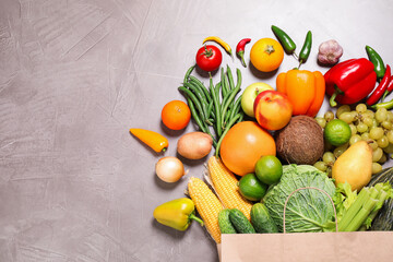 Paper bag with assortment of fresh organic fruits and vegetables on grey table, flat lay. Space for text