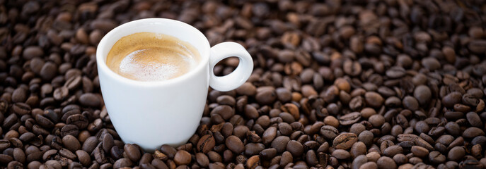 Flat lay with copy space, (selective focus) A white espresso cup with some creamy coffee is placed on some roasted coffee beans.