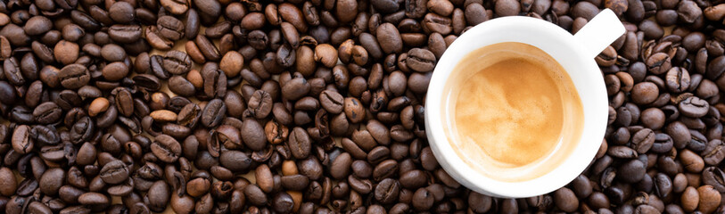 Flat lay with copy space, (selective focus) A white espresso cup with some creamy coffee is placed on some roasted coffee beans.