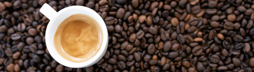 Flat lay with copy space, (selective focus) A white espresso cup with some creamy coffee is placed on some blurred roasted coffee beans.