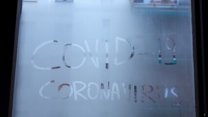 written Covid-19 Coronavirus on a fogged glass - hand erases the writing - concept of the end of the pandemic thanks to the arrival of the vaccine