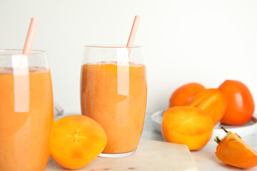Tasty persimmon smoothie with straw on marble board against white background
