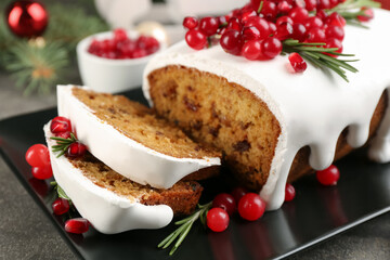 Traditional classic Christmas cake decorated with cranberries, pomegranate seeds and rosemary on black plate, closeup