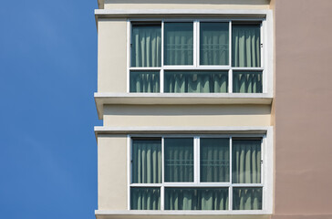 Fototapeta premium Modern building against a clear blue sky. Two glass windows with curtain..