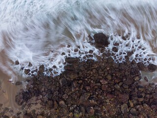 Aerial top view of sea waves hitting rocks.