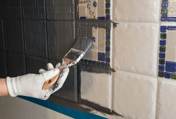Repainting old dated kitchen ceramic tile back wall with modern gray chalk paint indoors at home....