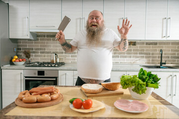 Emotional fat funny and tattooed man with food at the kitchen at home