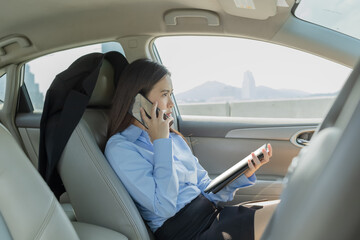 Businesswoman inside a car using a tablet and mobile phone for working.