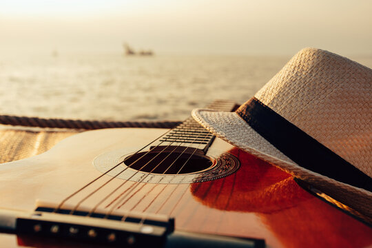 Guitar and hat on reed mat near the sea at sunset. Travel, vocation, holiday, summer concept.