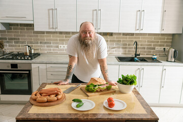 Emotional fat funny and tattooed man with food at the kitchen at home