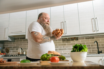 Emotional fat funny and tattooed man with food at the kitchen at home