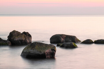 Fototapeta na wymiar Beautiful sunset over Baltic sea with stones in the water, long exposure photography. Tranquil scene.