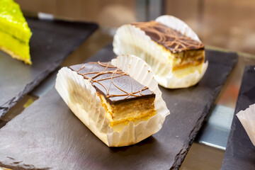 Pieces of bird's milk cake covered with chocolate lying on cafeteria shelf. Selective focus. Sweet food theme.