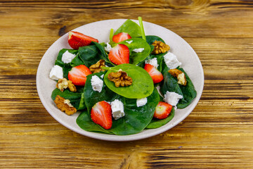 Fresh healthy salad with strawberry, spinach, walnuts and feta cheese on wooden table