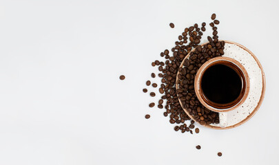 a coffee cup with roasted brown beans is scattered on a white table with plenty of room for text. Composition Of a flat layer. Close-up, top view, white background.